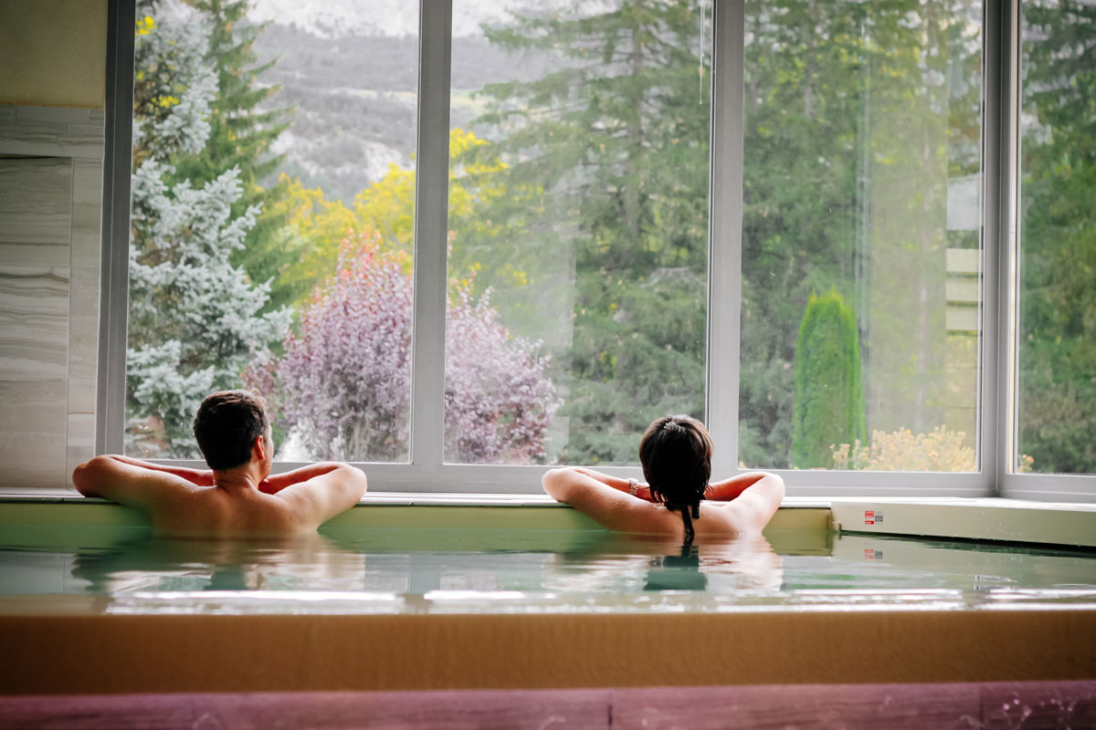 Couple détendu dans le bassin du spa face à la forêt et aux montagnes